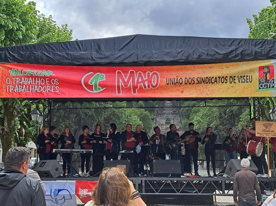 Grupo de Cavaquinhos num palco, com um banner da União dos Sindicatos de Viseu para o 1º de Maio, com o lema "Valorizar o trabalho e os trabalhadores"