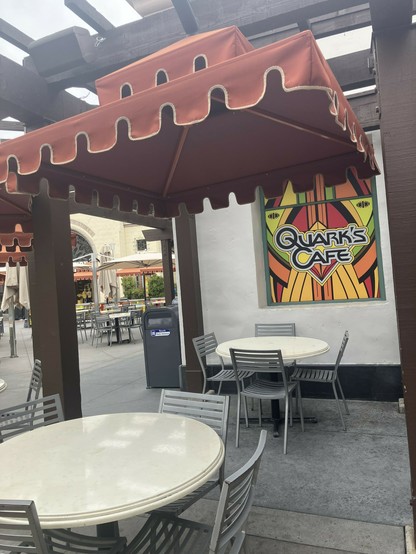 Photograph of a seat under a red awning with a brightly colored Quark’s Cafe logo.