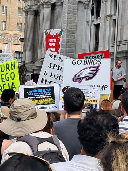 A crowd of protesters jam the streets in Philadelphia as they hold their protest signs.  One sign reads, "Return Abrego Garcia." Another reads, "For the People, Not Billionaires." Another has the Philadelphia Eagles logo and the words, "Go Birds, Dump Trump."