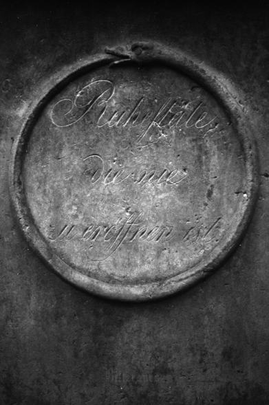 Black and white film photo of a gravestone with an ouroboros and the words "Ruhestätte, die nie zu eröffnen ist" ("resting place that is never to be opened")