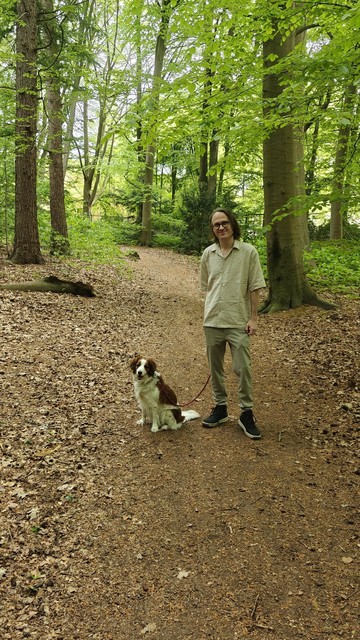 A nice green forest trail with in the center a guy (me) and a cute dog to the left of him posing for the photo