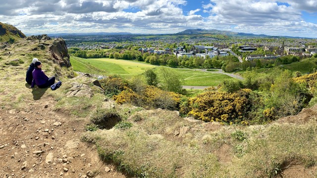Two lovers sitting atop Salisbury Crags in Hollyrood Park gazing at the green city of Edinburgh, Pentland Hills in the distance