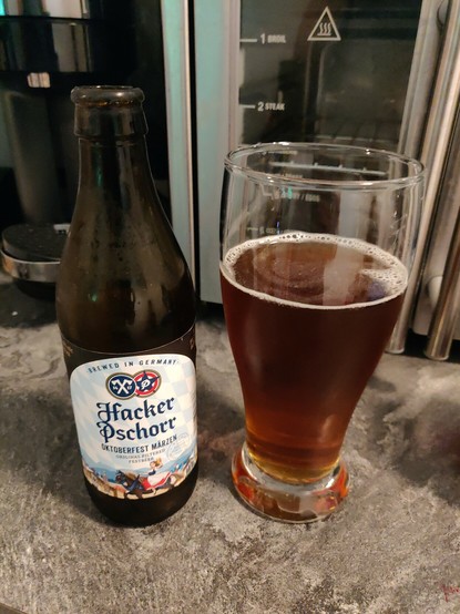 An open bottle of Hacker Pschorr Oktoberfest Märzen Beer with the contents of the bottle poured into the beer glass to the right of the bottle.