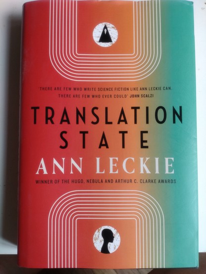 Photo of book, red/orange/yellow/green vertical fading in each other strips, "translation state Ann Leckie" written in the middle.
