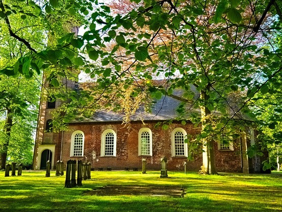 A pretty church with a lawn in front of it. There are various gravestones on it. Green leaves/trees can be seen everywhere. This reformed church was built in the 13th century and served as a burial place for members of the von Wedel family. At the end of the 13th century, the church was built with bricks in a monastery format as a hall church. In the 15th century, the cross-vaulted choir was added, extending the nave by 5.5 metres to the east across its entire width. A tower can be seen on the left, followed by the nave with white-framed arched windows.