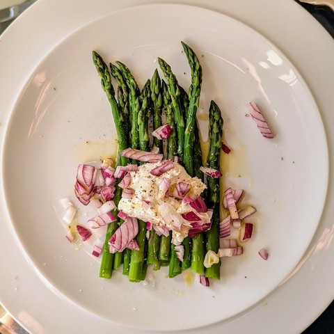 White plate, row of green asparagus spears, blob of white soft cheese, roughly chopped red onions scattered over