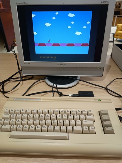 A Commodore 64G connected to a Samsung LCD monitor. A very basic, not working properly, sideways scrolling "endless runner" is on the screen.
