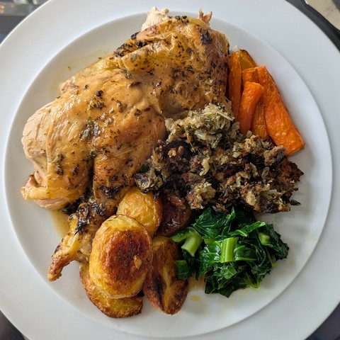 White plate, leg and wing of roast chicken, carrots, greens, roast potatoes, pile of stuffing, lots of gravy sluiced over