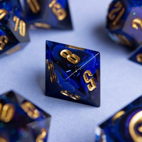 Ein D8 mit goldenen zahlen. Dahinter glitzert es und man sieht einen Farbwirbel aus Ultramarin, Schwarz und colorshifting mica.