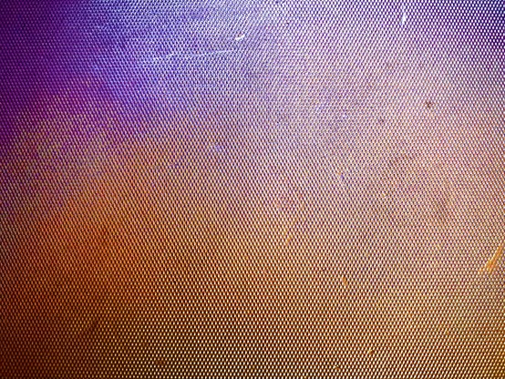 A rigid, bumpy, metallic surface reflects an array of light colors, such as purple, blue, orange, and yellow.