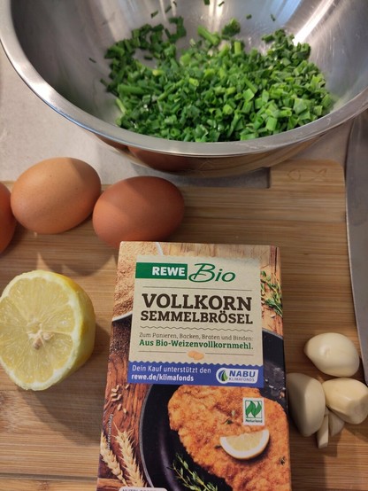 Ein paar der Zutaten für die Fischfrikadellen auf der Arbeitsplatte. Darunter Semmelbrösel, Knoblauch, Eier, eine halbe Zutrone und gehackter Schnittlauch
