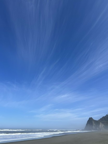 View from the coastal area of Redwood National and State Parks today. The blue sky is a welcome sight. The addition of elegant flowing cloud forms is an added benefit. In the foreground, the Pacific Ocean meets the shore. The point in the distance is about a four mile walk round trip from the closest trailhead.