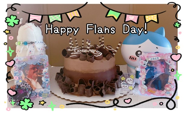 A picture of a set up of various John Flansburgh themed items. A cake is in the center, with Happy Flans Day in a caption across the top.