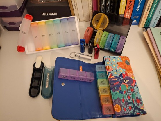 Ein Foto von mehreren verschiedenen Pillen-Dosen und -Organizern.
Drei davon haben einzeln entnehmbare Behälter mit aufgedrucktem Wochentag, und sie sind in mehrere Abteilungen für verschiedene Medikamenten-Dosen am Tag unterteilt. Ausserdem sind sie bunt.