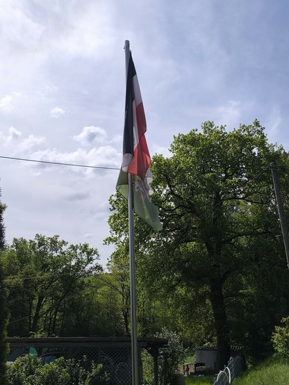 Auf diesem Foto sieht man, an einem Fahnenmast, zwei Fahnen. Die obere Fahne ist eine Reichsfahne, die untere Fahne ist die Fahne der rechtsradikalen Partei "Freie Sachsen"