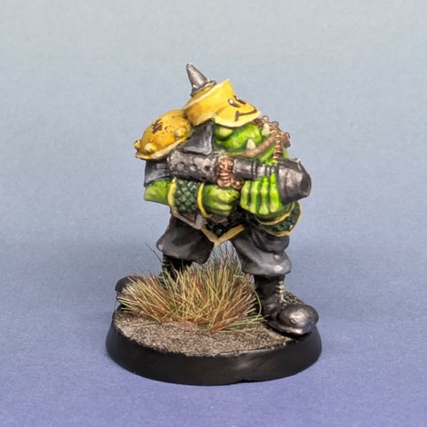 An ork with a yellow hat with spike on top and smoky face on the brim. He's pointing a gun and has a yellow shoulder pad.