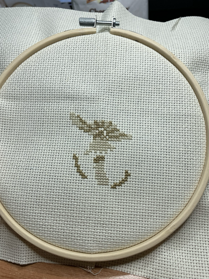 An in progress snapshot of a cross stitch patter that depicts the stem of two small mushrooms and a larger mushroom in light beige and darker beige.