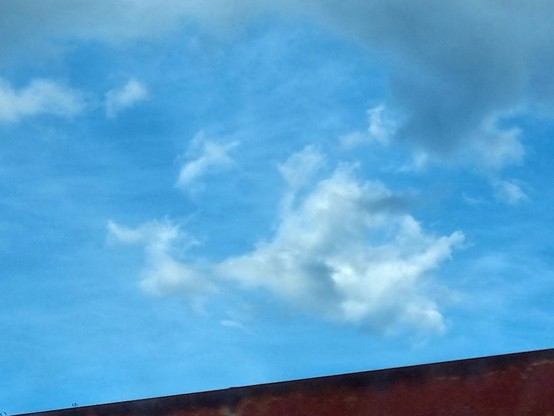 Nel cielo azzurro, sopra un tetto, una nuvola sembra avere la forma di un dragone