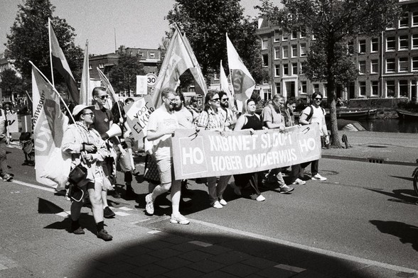 B&W image worker unions demonstrating on May first slogan on sign ¨Voor Elkaar" (for each-other ), banner "Kabinet sloopt hoger onderwijs¨ (kabinet destroys higher education), flags with AKKU, student workers union