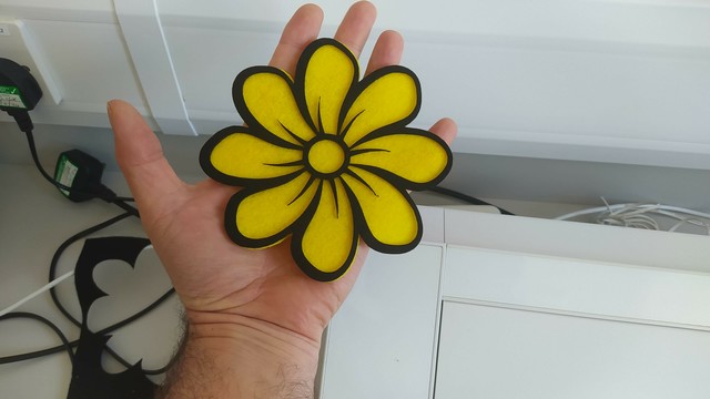 My hand holding a bright yellow flower made from 2 layers of felt.