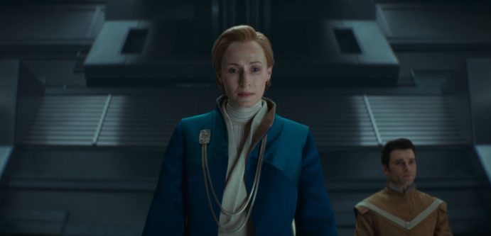 Capture écran série Andor Saison 2: Mon Mothma interprétée par l'actrice Geneviève O'Reilly au Sénat galactique sur sa plateforme avec son assistant dans le fond