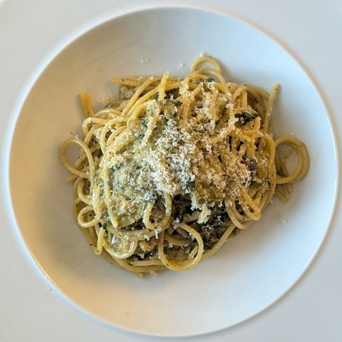 White bowl with a tangle of spaghetti and dark green smashed up courgette, lots of parmesan grated over
