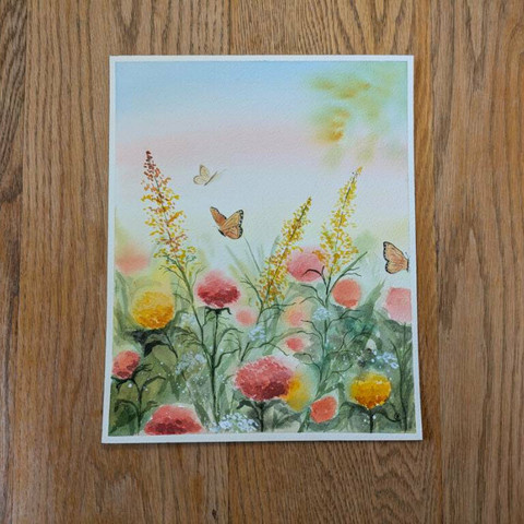This is a watercolor painting of a portion of a butterfly garden. It's in portrait orientation. The sky starts out blue at the top and fades to pink and then a pale golden. In the top right corner there is a blurry tree branch of leaves. The garden itself has some blurry red, orange, and yellow globe like flowers. The grass and leaves are also blurry to create depth among the flowers. In the foreground, the flowers are more detailed with color variation from dark to lighter speckling and the stems and leaves are crisp and darker. There are some Queen Anne's Lace among the lower half of the painting. There are three stocks of goldenrod reaching towards the sky at various angles.  To complete this painting are three monarch like butterflies among the flowers.
