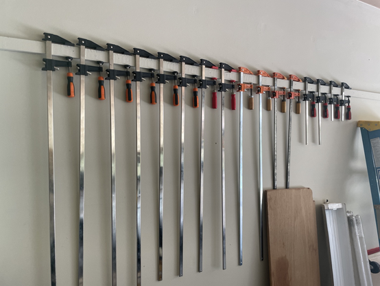 A wall in a garage with wood clamps hanging in size order