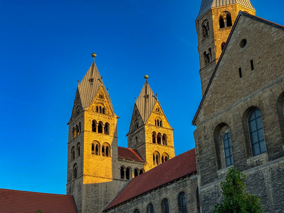 Eine von der Morgensonne angestrahlte Kirche (Liebfrauenkirche Halberstadt) vor tiefblauem Himmel, dazwischen rote Ziegeldächer