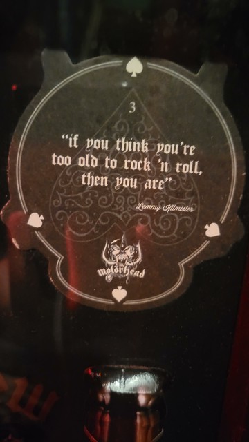 Image of a coaster with a quote from Lemmy of Motörhead. It says "If you think you're too old to rock 'n roll, then you are." The coaster features a Motörhead logo at the bottom, and 4 Spades surround the outer edge.