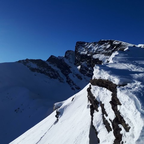 Fotografía de un paisaje montañoso y escarpado, cubierto de nieve en su mayor parte, bajo un cielo totalmente despejado.