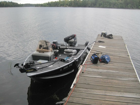Black fishing boat tied uo to a wooden dock on a cloudy day.
