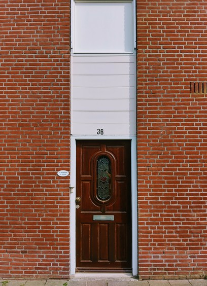 Bakstenen gevel met bruine voordeur in een wit raam met daarboven een venster ¦ Brick facade with a brown front door in a white frame with above a window