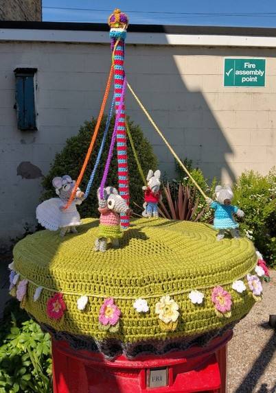 Four mice, from the Marvellous Mechanical Mouse Organ, are dancing around a Maypole on top of a pillar box.