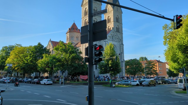 Photo von einem Flohmarkt. Im Vordergrund eine Straßenkrruzung, dahinter die Wiese mit vielen Menschen und Flohmarkt-ständen rund um die Kirche St. Adalbero