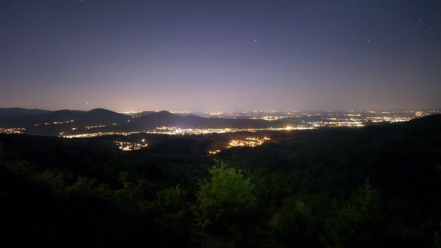 Leuchtende Bänder aus Häusern und Straßen in der Nacht in einem weiten Tal, gesehen von oben.