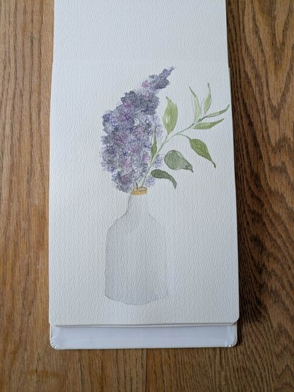 This is a watercolor and mixed media painting of one branch of lilac and leaves in a white ceramic single stem vase, rimmed in gold with a narrow neck. The composition is sketched out in graphite with loose bluey gray ish purple watercolor making up the shape of the lilac. Then I added cool purple and warm purple colored pencil to build up the tiny floral clusters. The branch, while seemingly straight leans right towards the top.  The messy loose leaves take up the upper right half of the competition in tones of yellow green and graphite. The vase is center left to give the painting balance.