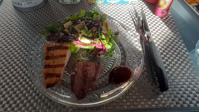 Ein Glasteller mit zwei Stücken Fleisch etwas Soße und einen frischen Blatt-Apfel-Salat.