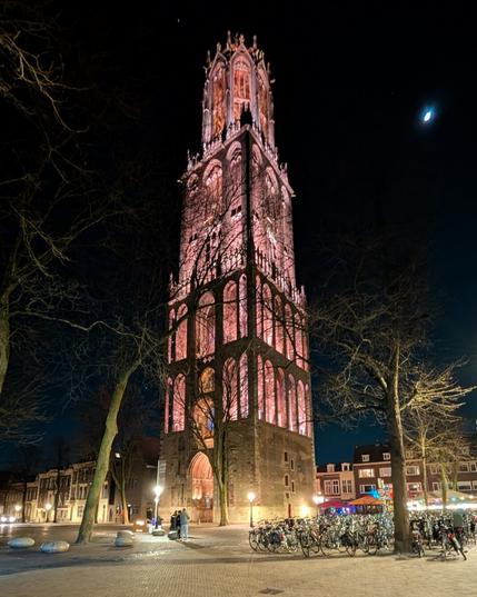 Free standing church tower at night, with loads of yellow and pink lighting. Photographed from a distance.