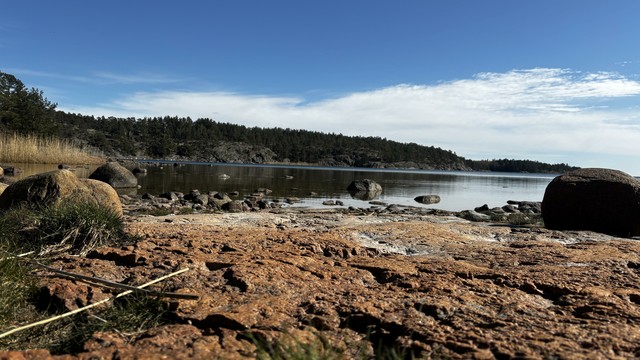 View from a red granite beach out over the water and the hills on the other side.