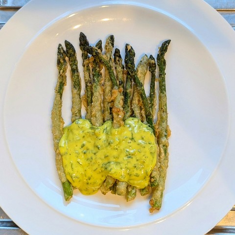White plate, row of lightly battered asparagus spears with a large pool of bright yellow, green-flecked mayonnaise