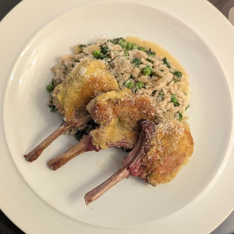 White plate, three breaded lamb cutlets on the bone sitting on a pile of pale fat rice mixed with peas and herbs, light dusting of parmesan