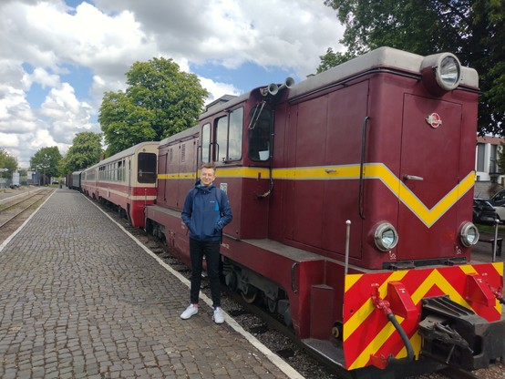 A skinny boy standing in front of an Lxd2 loco, waiting for its departure from Piaseczno Miasto station. The loco is pulling three Romanian-made Bxhpi passenger cars, a green restaurant car and a single freight car with some equipment.