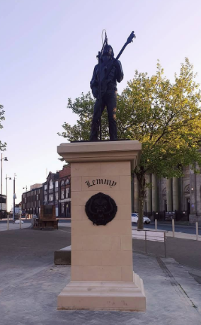 A statue of legendary heavy metal frontman Lemmy Kilmister, in his iconic pose: guitar in hand, in front of a tall mic.