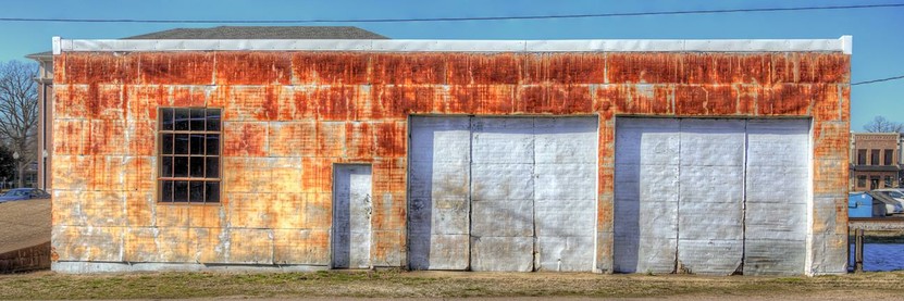 A weathered, rust-colored brick building is featured with two large, white garage doors and a single window.