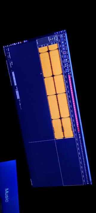 The photograph shot in total darkness shows a computer screen displaying a digital audio workstation (DAW) interface. The screen is tilted at an angle, with a dark blue background. The main area of the screen features a grid with orange blocks, likely representing audio clips or regions. These blocks are arranged in a vertical column, with some having black vertical lines indicating the waveform of the audio. The top of the screen includes various controls and buttons, such as "Edit," "Select," "View," and "Transport," along with a timeline on the right side. The bottom left corner of the screen has the word "Music" in light blue text on a dark blue background. The overall layout is typical of a DAW, with a focus on editing and arranging audio tracks.

 Ovis2-8B

🌱 Energy used: 0.195 Wh
