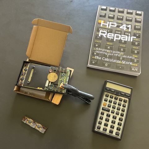 A cannibalized HP-41 calculator next to a working model and a repair book.