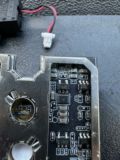 Close-up of a circuit board featuring various electronic components, including resistors and capacitors. A connector and wiring are visible, indicating connections for power or data. The surface appears slightly worn or dirty.