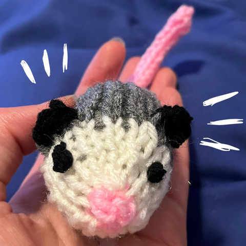 A close-up of a tiny knitted opossum, as if he's sniffing the camera