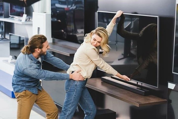 Angry boyfriend pulling girlfriend with tv in home appliance store